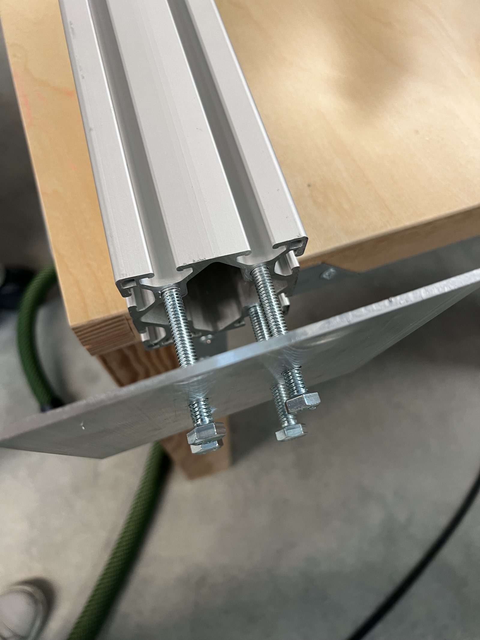 An 8020 aluminium mast joined to a steel base plate via threaded studs — the drilled and tapped result