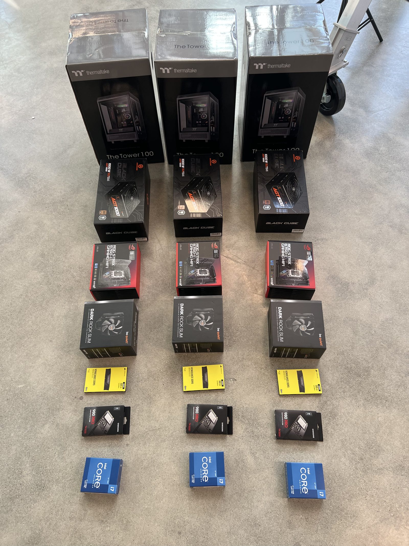 Three sets of PC components laid out in their boxes — chassis, GPUs, coolers, fans, SSDs, CPUs